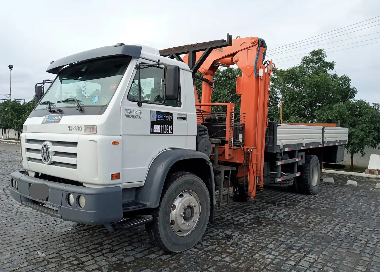 Caminhão munck toco 4x2 da Becker Ferreira, lança laranja recolhida atrás da cabine e carroceria de madeira vazia