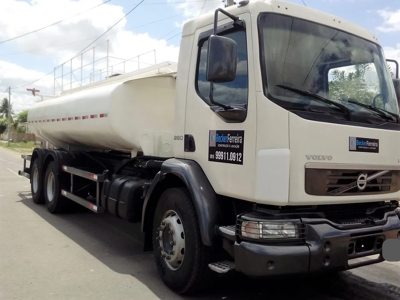 Caminhão pipa Volvo da Becker Ferreira, tanque de água em aço sobre chassi de três eixos, parado em via asfaltada